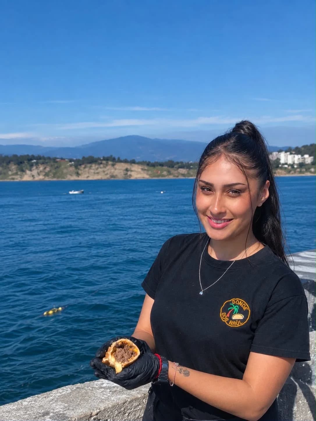 Integrante del equipo de Empanadas Don Raúl sosteniendo una empanada recién hecha junto al mar.